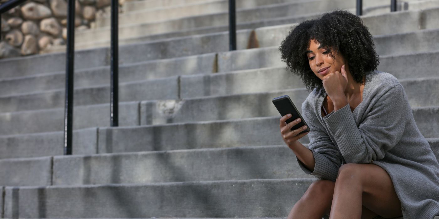Woman reading smartphone seated on outdoor steps.
