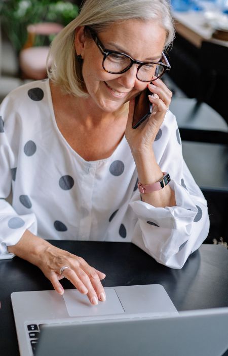 Woman on phone using laptop at desk.