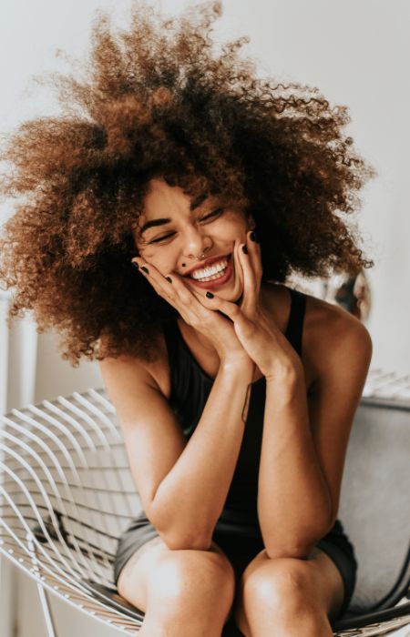 Smiling woman with curly hair, seated on chair.