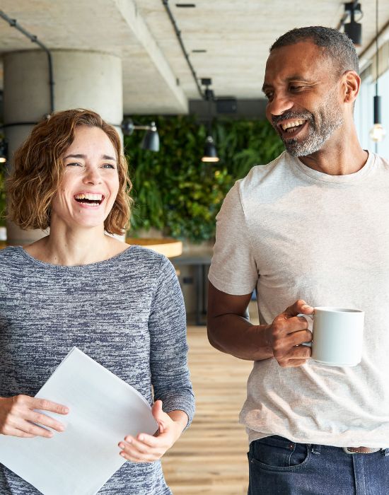 Two people laughing with coffee in office.