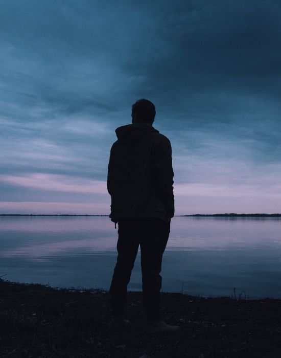 Person standing by a lake at twilight.