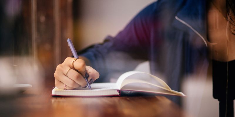 Person writing notes in a notebook at desk.