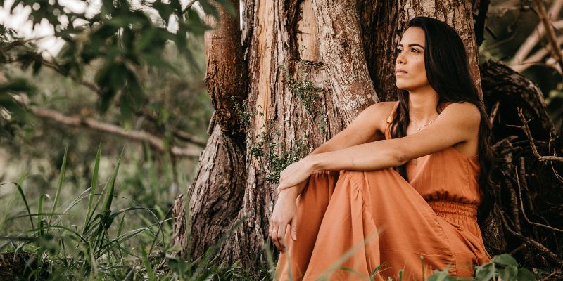 Woman in orange dress sitting by tree