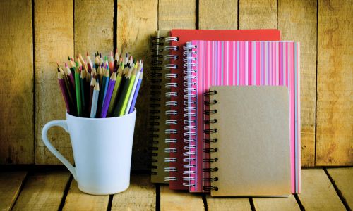 Colorful pencils and notebooks on wooden background.