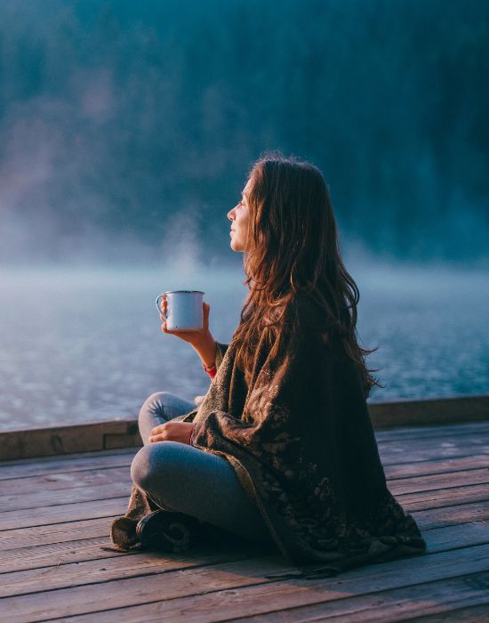 Woman relaxes with coffee by the lake.