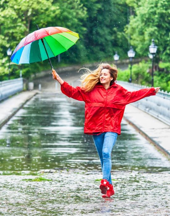 Woman dancing in rain with colorful umbrella.